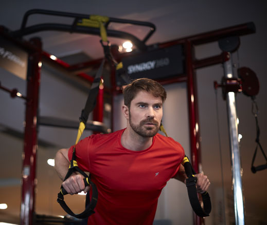 Image of man using the TRX strap on the synrgy unit in the gym