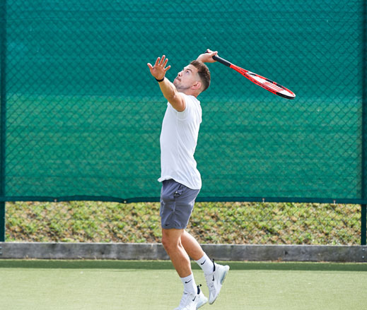 Image of man hitting a serve on an outdoor tennis court
